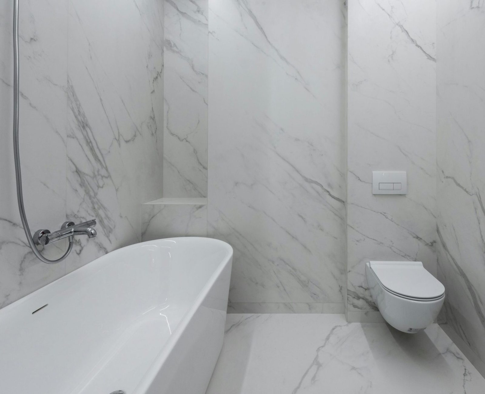 Interior of stylish bathroom with marble walls and bath placed near toilet and ceramic sink in light room with mirror